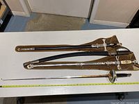 Three ornate daggers with scabbards and fencing sabre on table