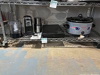 Overview of all small appliances on metal shelf including Patriots Crockpot, K-cup drawer, Cuisinart spice and nut grinder, Hamilton Beach electric can opener, Cuisinart Food Processor, and electric griddle.