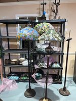 Three floor lamps with shades displayed in front of shelving holding additional shades