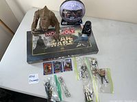 Overview of all items on white table: 5 Star Wars figures in bags, 3 Shadows of the Empire trading cards, sealed Monopoly Star Wars board game, Darth Vader and creature Pez dispensers