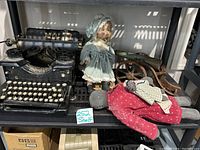 Lot arranged on shelf, includes typewriter, 3-sided face doll, miniature cannon, and rag dolls visible.