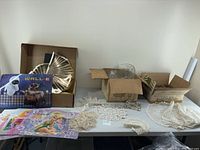 Wide view of lot showing vintage crocheted doilies spread out on table, packed boxes possibly containing glassware, and colorful Disney-themed placemats