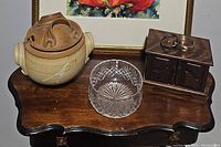 Overview of all items on a wooden table; includes ceramic soup dish, cut crystal dish, wooden jewelry box, and two bracelets on top of jewelry box.