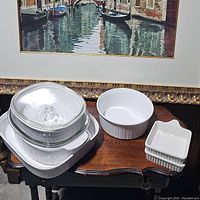 Photo showing multiple white ceramic bakeware dishes including rectangular, round with glass lid, and smaller square dishes stacked.