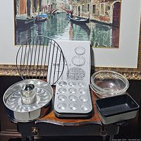 Photo showing assortment of baking pans and rack on a wooden table with decorative painting in background.