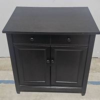 Front view of black wooden cabinet showing closed drawer and double doors.
