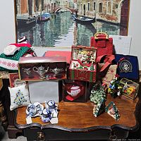 Wide photo of assorted Christmas decorations on wooden table including miniature tea sets, Christmas ornaments, figurines, decorative boxes, and holiday cloth items.