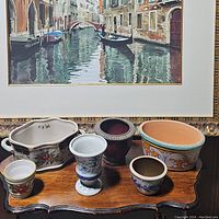 Overview of all six decorative pots arranged on a wooden surface in front of a framed picture.