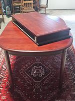 Dining table with one leaf extension resting on top showing rounded corners and wood finish.