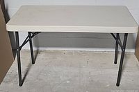 Full view of folding table with white plastic top and black metal legs.