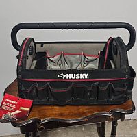 Front view of the Husky tool bag showing the logo, handle, and multiple external red-piped pockets.