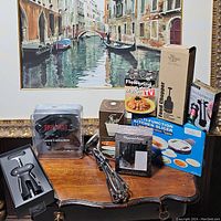 Photo showing all kitchen gadgets on a wooden table with a large Venice canal painting in the background.