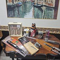 Full lot of assorted kitchen tools and accessories laid out on wooden table under framed print