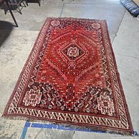 Full view of the rectangular red Persian-style rug showing central medallion and border pattern, laid on concrete floor.