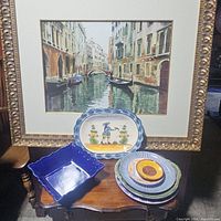 Overview of assortment including several plates and a blue bowl with a framed artwork in the background