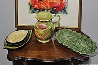 Full view of assortment showing three leaf-shaped trays stacked, one embossed green rectangular tray, and hand-painted pitcher.