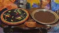 Group of serving pieces including ceramic platters, metal tray, and small wooden dish displayed on wooden table.