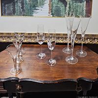 Wide shot showing all nine stemware placed on a wooden surface with a framed painting in background.