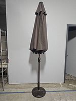Full view of the closed brown patio umbrella on stand.