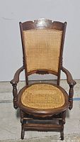 Front view of vintage rocking chair showing rattan seat and back with carved wooden frame and armrests.