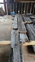 Four weathered barnboards stacked horizontally inside a barn, showing rough wood texture and edges