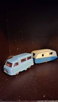 Photo showing antique light blue toy van and matching cream and blue toy trailer positioned side by side on a dark background.