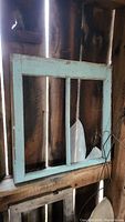Antique wooden window frame painted light blue, showing weathered paint and broken glass panes with two vertical dividers.