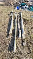 Four long cedar beams laid on grass outside showing rough natural wood texture and squared ends