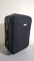 Front and side view of black carry on luggage showing metal brand plate and structured rectangular shape.