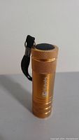 Front view of gold Kubota flashlight standing upright, showing textured grip, brand name, and black button at top.
