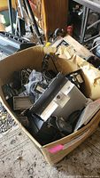 Large cardboard box filled with various electronic devices and components including a large electronic unit with cooling fins and cables
