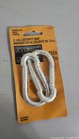 Two galvanized metal Everbilt security snap clips in unopened orange and black packaging labeled with size 3-1/8 inch and weight rating 353 lbs