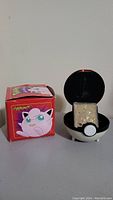 Photo showing gold plated Jigglypuff Pokemon trading card inside Pokeball holder alongside original red box