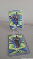 Two Shaquille O'Neal promo basketball cards, one standing on a display stand, both with holographic green-blue-yellow background and O'Neal in black Cole #33 jersey
