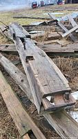 Photo showing full length of the large weathered barn beam laid on the ground with multiple mortise cuts and wooden peg holes visible.