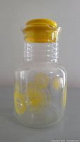 Front view of the clear Pyrex glass pitcher with yellow lemon decoration and yellow plastic lid