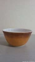 Side view of vintage Pyrex Old Orchard mixing bowl showing orange to yellow gradient exterior and white interior visible at rim.