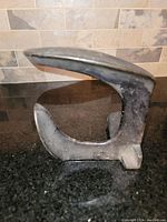 Side angle showing the curved horn and flat base on a black granite surface with a stone tile background.
