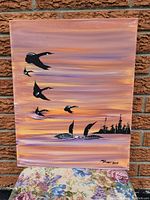 Front view of the original painting by Randy Knott against a brick wall. Shows the full canvas with loons flying and swimming.