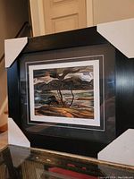 Photo of framed fine art print titled 'Bent Pine' by A.Y. Jackson in black frame with protective corner guards, angled view.