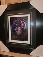 Front view of the professionally framed art print depicting an abstract colorful human face titled 'Soothsayer'. Frame is black with double matte border around the print.