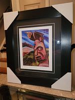 Angled photo of the professionally framed Emily Carr "Thunderbird" print showing protective corner covers on the black frame and visible white and black matting around the colorful totem pole print.