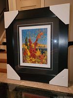 Framed fine art print by Tom Thomson titled 'Autumn Foliage' with protective corner pads still on the frame, showing front overall view.