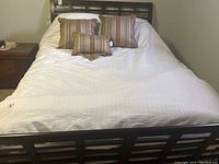 Bed with white duvet and cover, multiple brown/beige striped decorative cushions arranged on bed