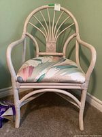 Front view of a light cream wooden patio style chair with curved back and armrests, floral seat cushion.