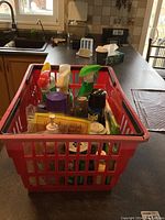 Red plastic basket filled with various spray bottles and cleaning products on kitchen counter, showing overall contents of cleaning tote.