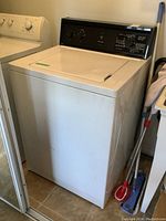 Full front-left view of white Kenmore washer next to dryer and cleaning tools.
