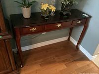 Wooden couch table with three drawers. Dark wood finish, polished top, brass handles on the drawers, curved cabriole legs.