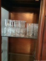 Crystal stemmed wine glasses and stemless glasses with different cut glass patterns displayed on glass shelves.