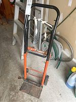 Front view of the adjustable dolly hand truck showing the black and orange frame with handle and fabric strap tied on.